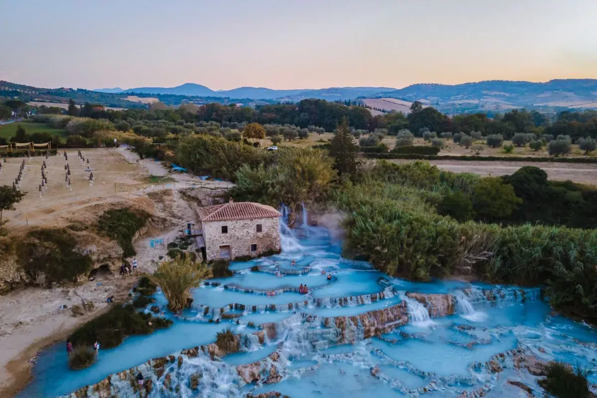 Cascate termali con acqua azzurra e un vecchio mulino, un'oasi di relax che ricorda le terme a Firenze.