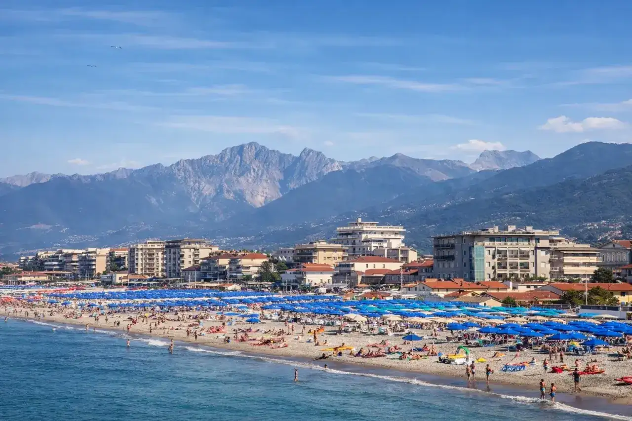 Una vivace spiaggia libera al Lido di Camaiore, con montagne imponenti sullo sfondo e un mare azzurro.