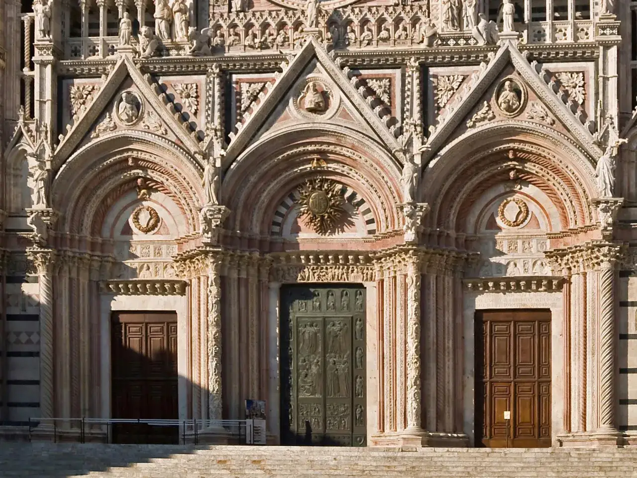 Dettaglio della facciata del Siena Cathedral con tre portali, decorazioni scultoree e marmi policromi.