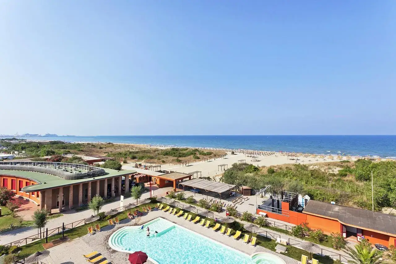 Un resort con piscina e spiaggia attrezzata, con il blu del tirrenia mare all'orizzonte.