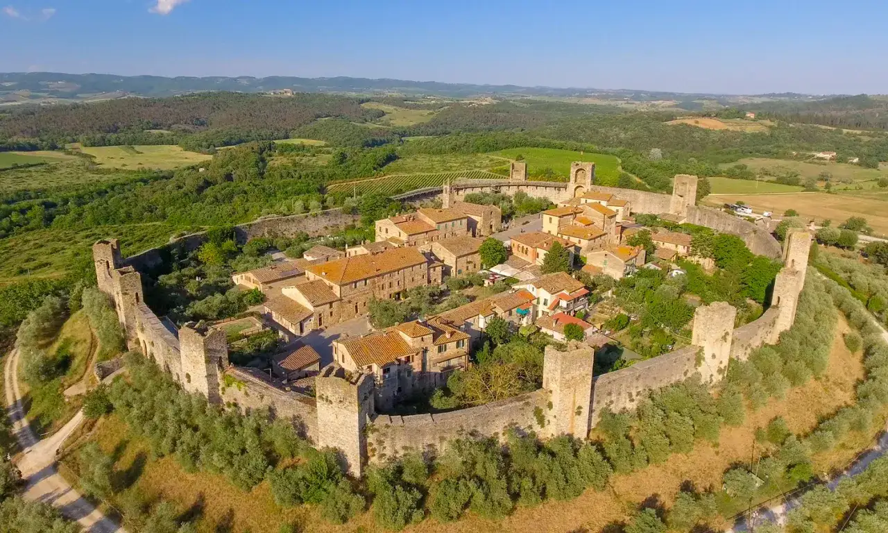 Borgo medievale di San Gusmè, con mura fortificate e torri, immerso nel paesaggio collinare toscano.