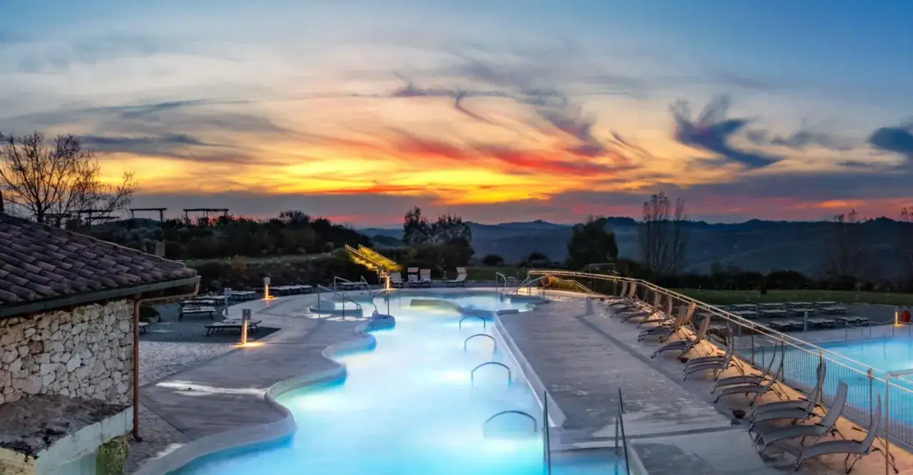 Piscine illuminate al tramonto in un thermal spa tuscany, con colline ondulate sullo sfondo.
