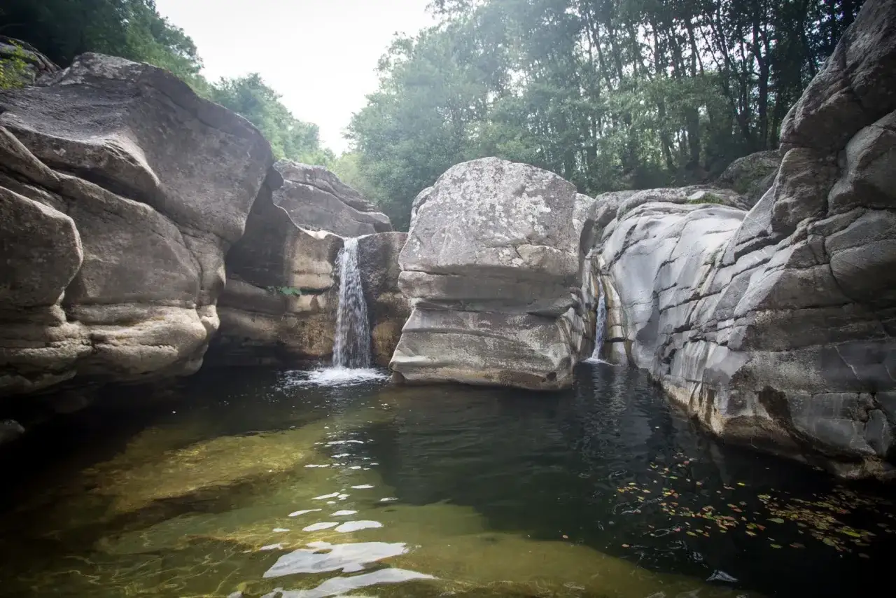 Cascate naturali nella riserva naturale Farma, con rocce levigate dall'acqua e vegetazione lussureggiante.