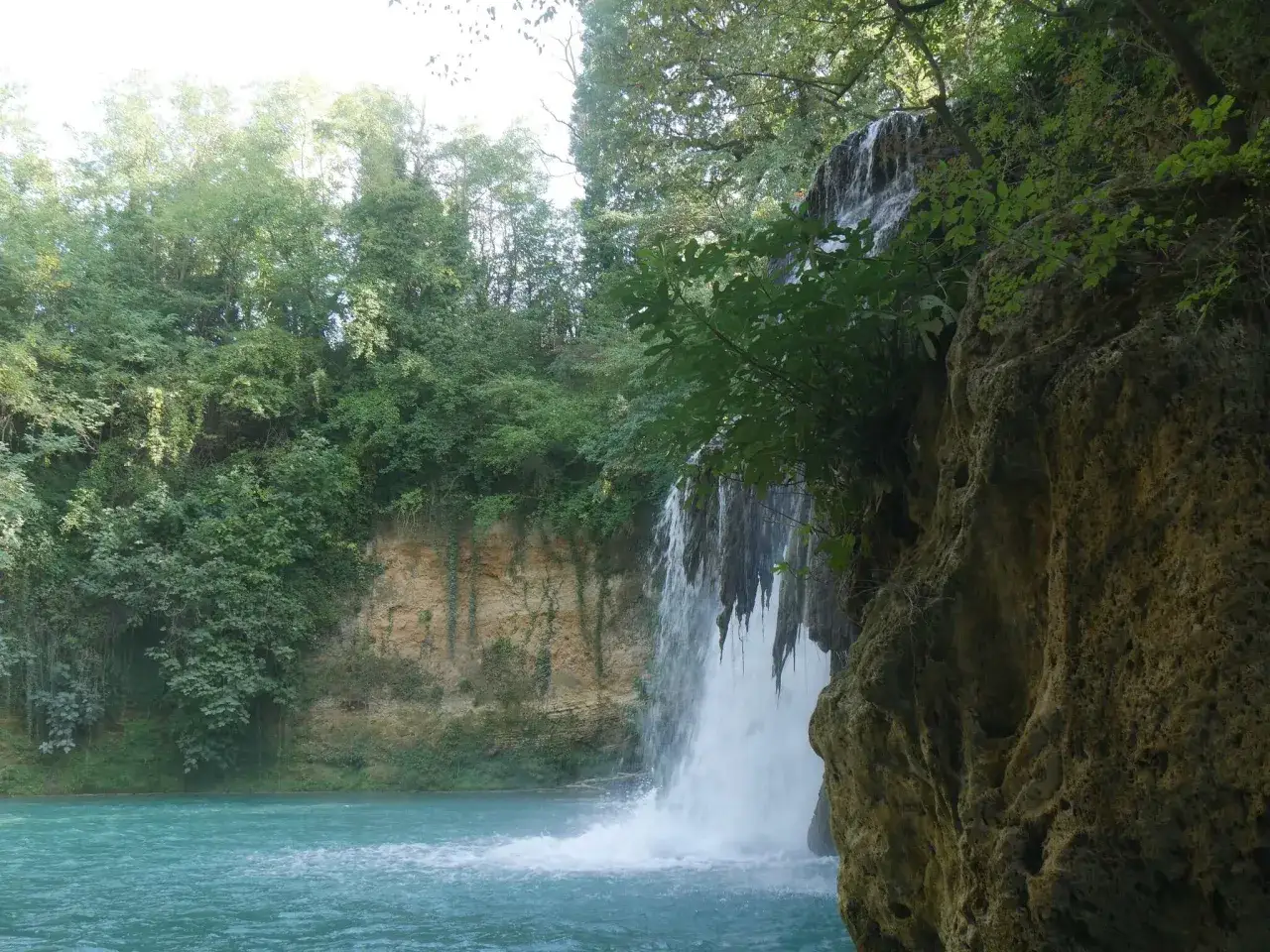 Cascata nel Val d'Elsa, con acque turchesi e vegetazione lussureggiante che incornicia la roccia.