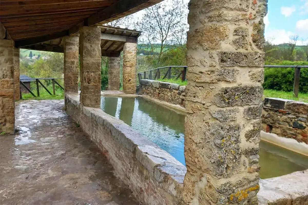 Antiche vasche termali nel centro storico di San Casciano dei Bagni, con colonne in pietra e tettoia in legno.