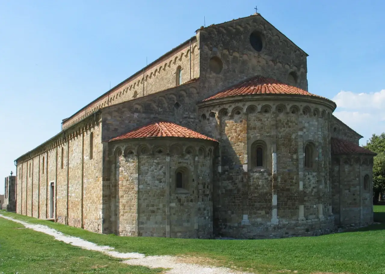 Basilica romanica di San Piero a Grado, con le sue absidi semicircolari e il tetto in tegole rosse, immersa nel verde.