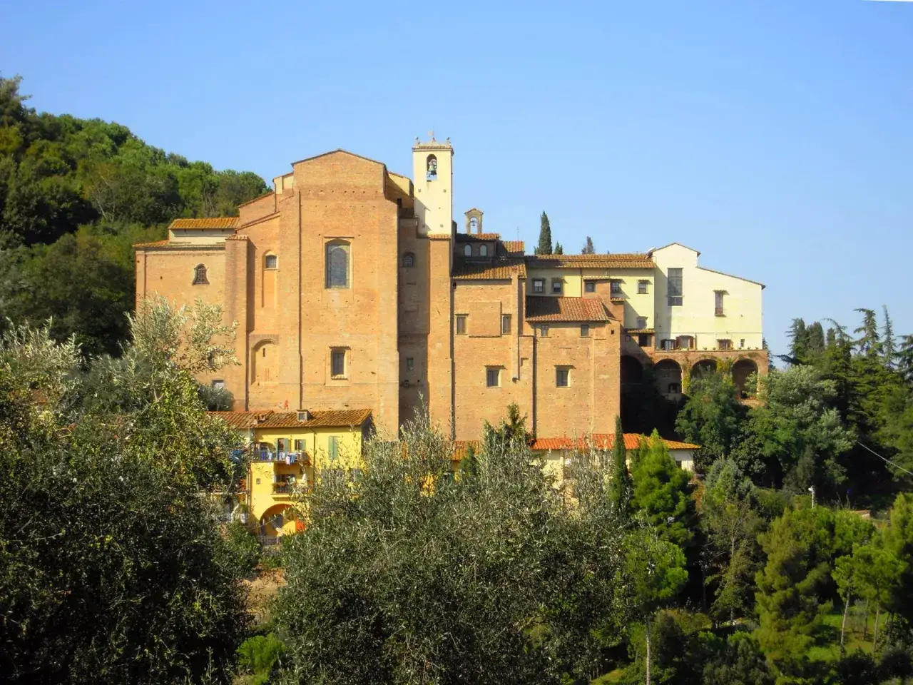 Il convento San Francesco a San Miniato, con la sua imponente struttura in mattoni rossi, si staglia tra il verde degli alberi e il cielo azzurro.
