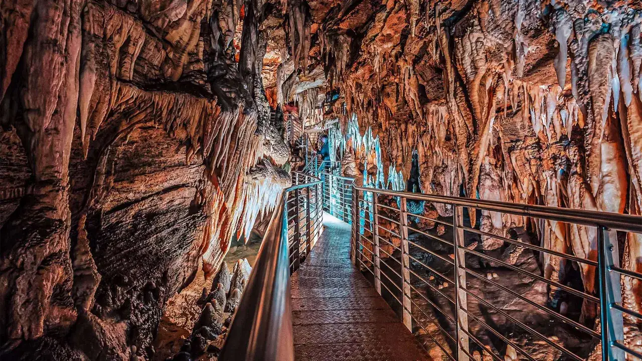 Sentiero illuminato nella grotta turistica Antro del Corchia, tra stalattiti e stalagmiti colorate.