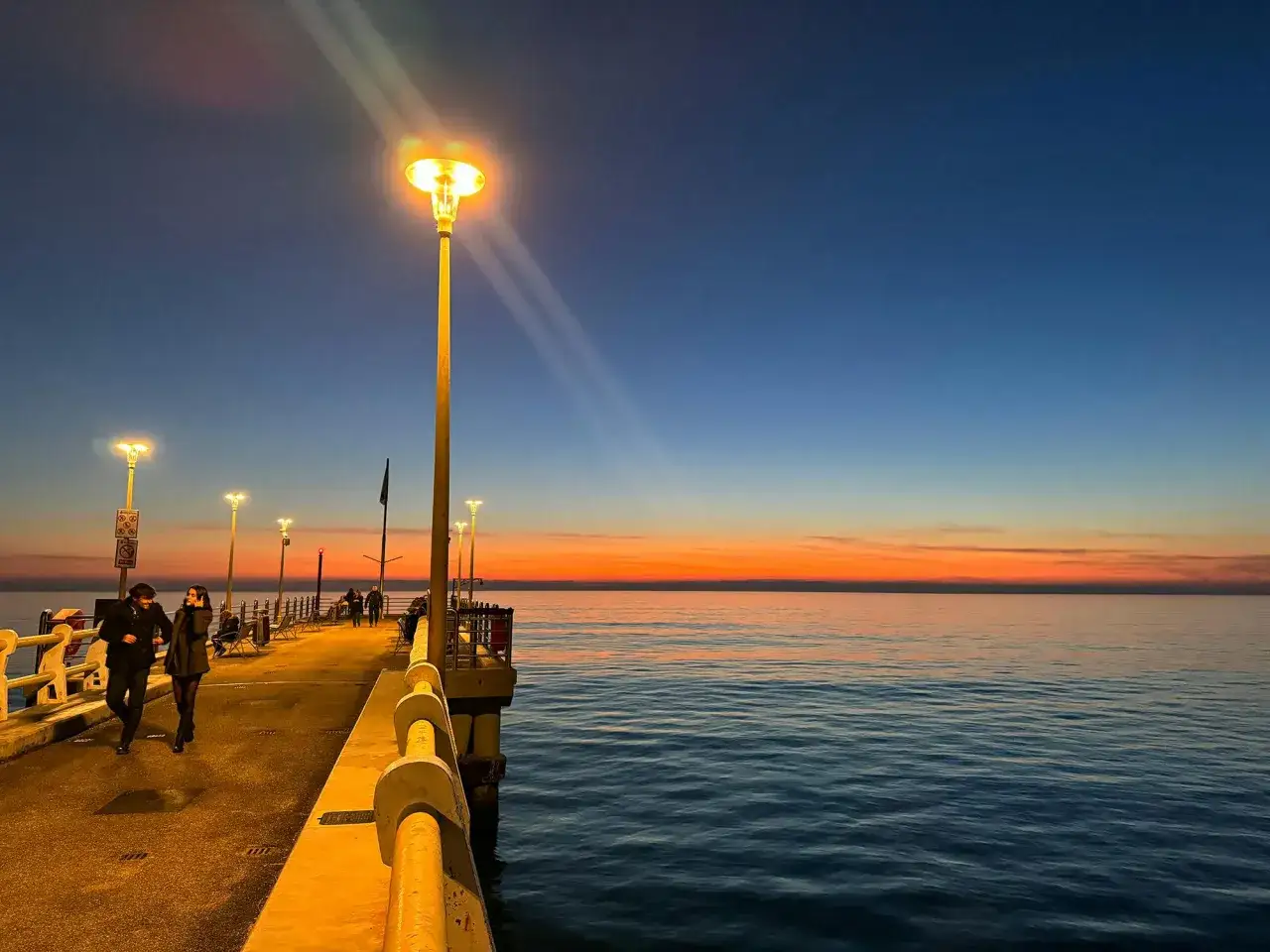 Passeggiata serale sul pontile di Forte dei Marmi, con luci accese e un tramonto infuocato sul mare.