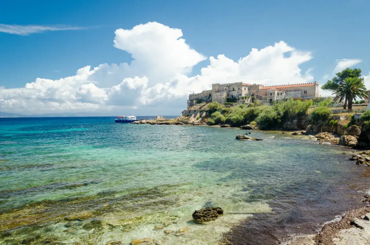 Costa rocciosa con un antico edificio storico sull'isola di Pianosa. Acque cristalline e un traghetto blu all'orizzonte.