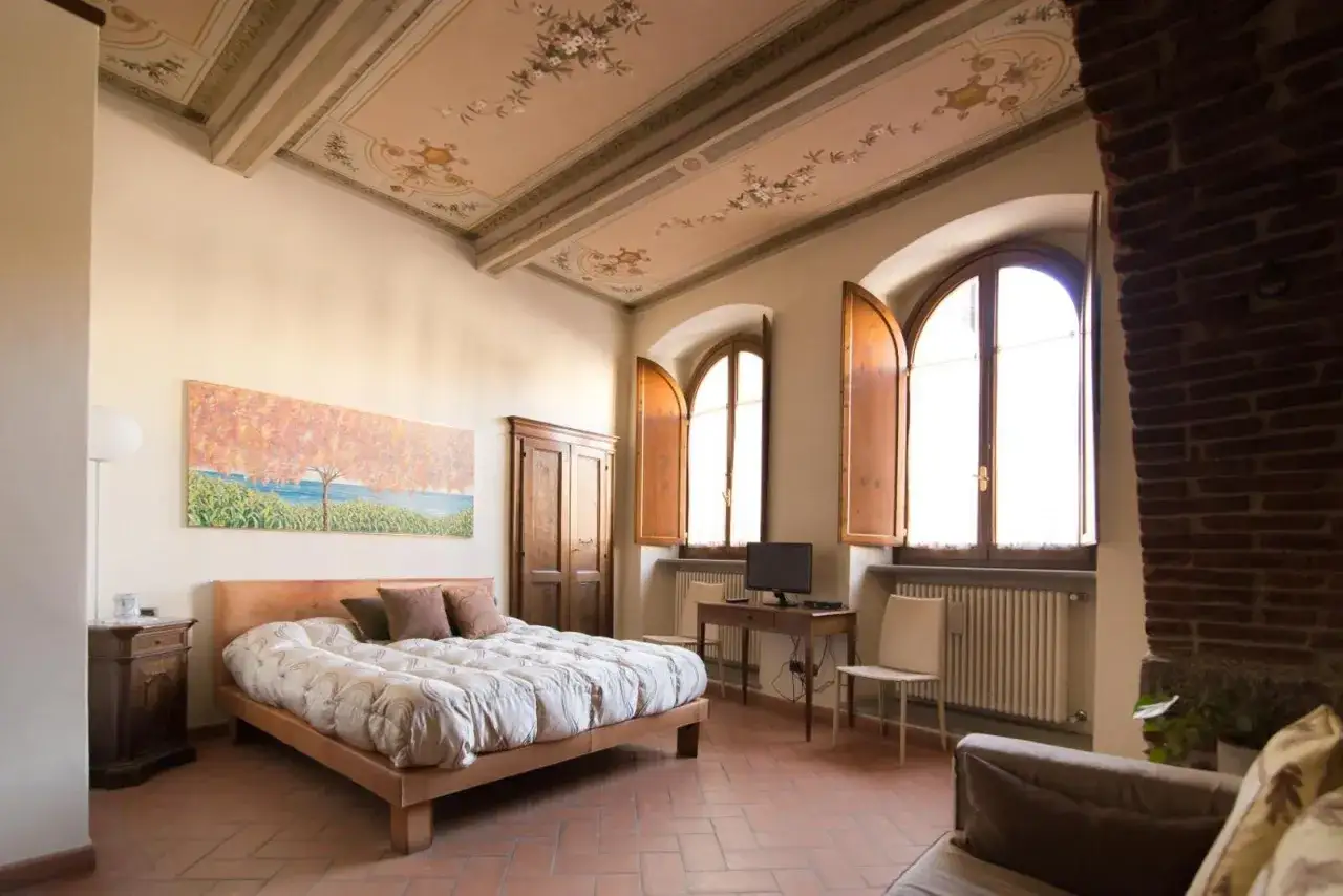 Camera accogliente con soffitto affrescato, ideale per chi cerca dove dormire ad Arezzo. Letto comodo, quadro colorato e finestre con persiane in legno.