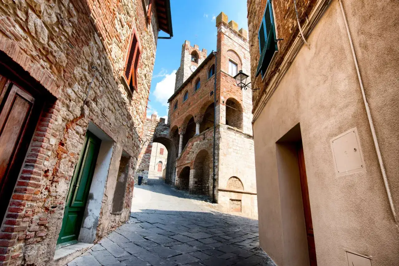 Un vicolo lastricato a Suvereto, Livorno, con edifici in pietra e mattoni, un arco e una torre medievale.