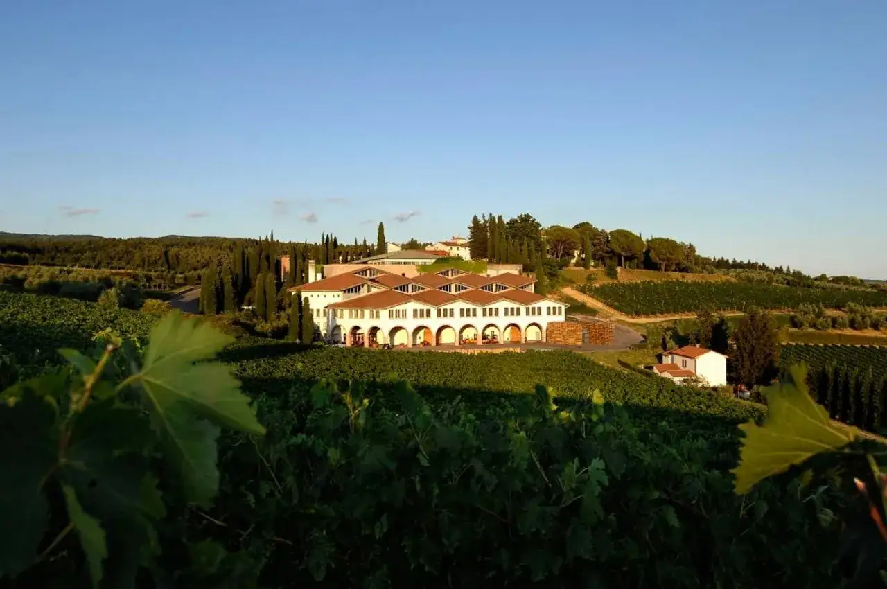 La cantina Melini si staglia tra le dolci colline toscane, circondata da rigogliosi vigneti sotto un cielo azzurro.