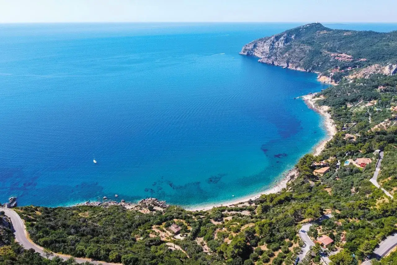 Vista aerea di una baia con acque turchesi e una costa verdeggiante. Perfetto per scoprire cosa vedere a Porto Ercole, tra ville e sentieri panoramici.