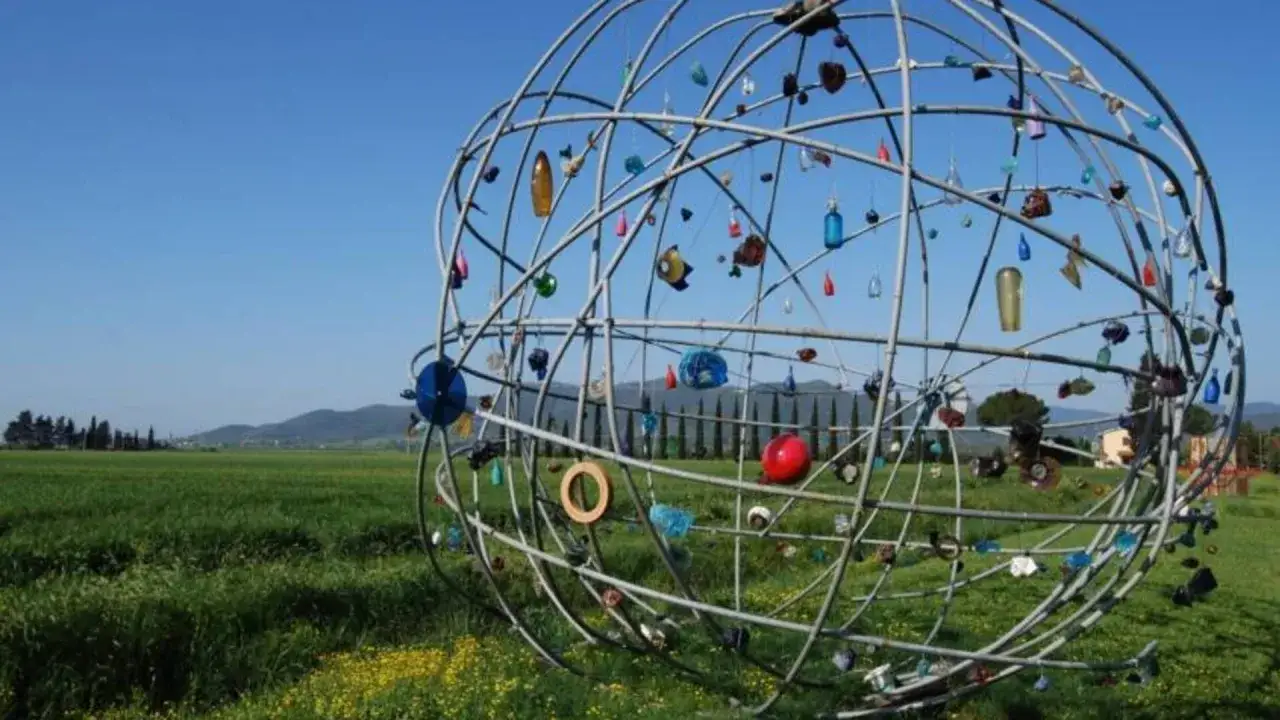 Scultura sferica con oggetti colorati appesi, in un prato verde. Un ricordo del giardino viaggio di ritorno.