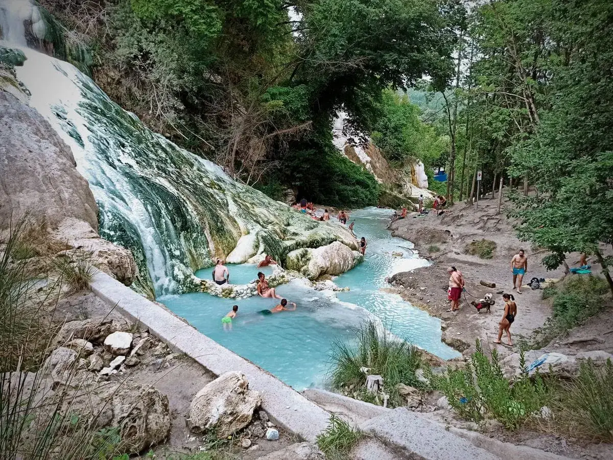 Cascata termale con gente che si rilassa nelle acque azzurre, un angolo di paradiso alle terme di Abbadia San Salvatore.