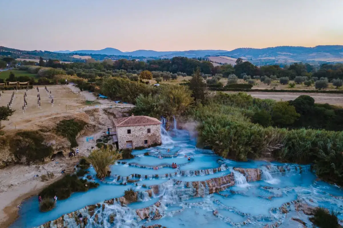 Cascate termali con acqua azzurra e un antico mulino, un'oasi di relax che ricorda le terme a Firenze, immersa nel verde della campagna toscana.
