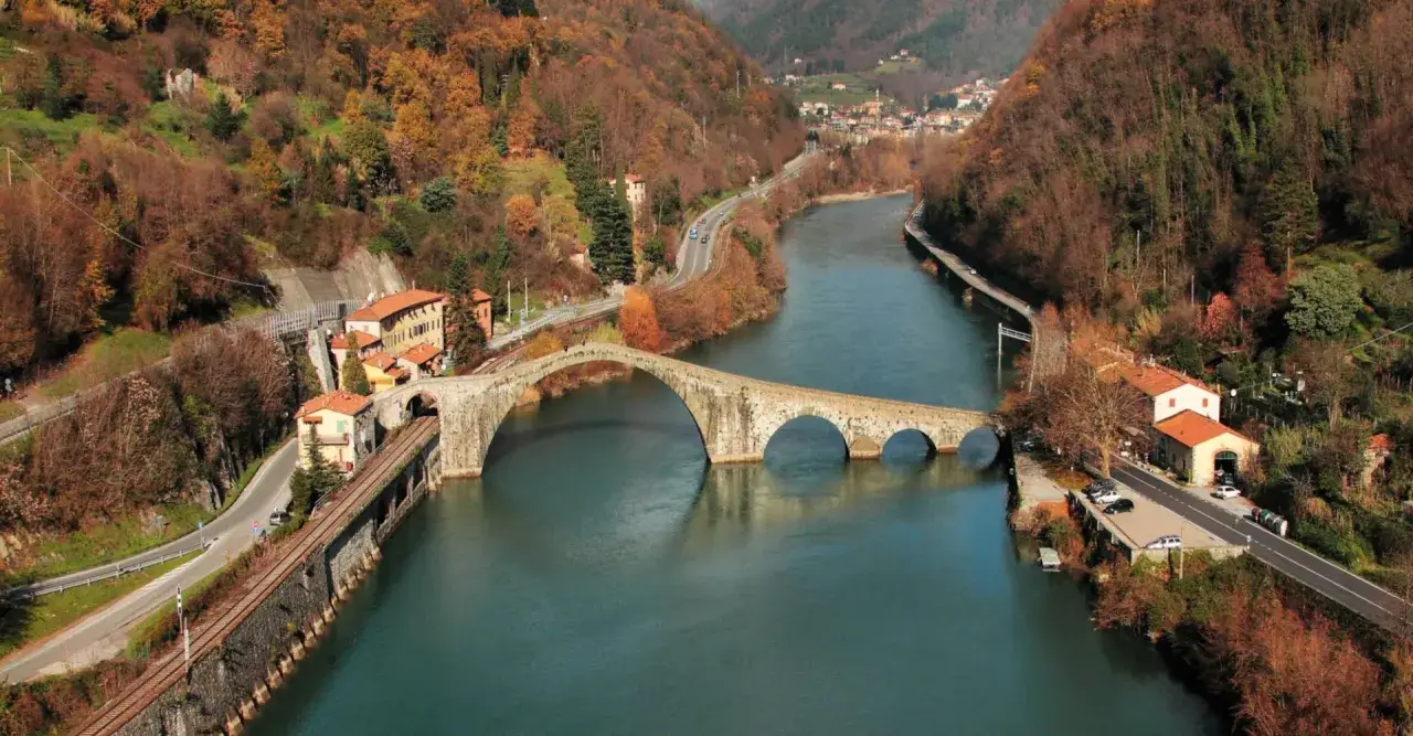 Ponte del Diavolo, un'antica meraviglia in pietra che attraversa un fiume, circondato da colline autunnali e case pittoresche.