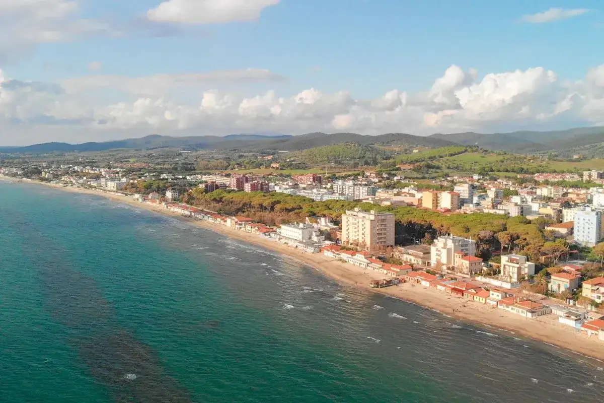 Vista aerea di Follonica mare, con la spiaggia dorata, il mare azzurro e la citt&agrave; che si estende verso le colline verdi.