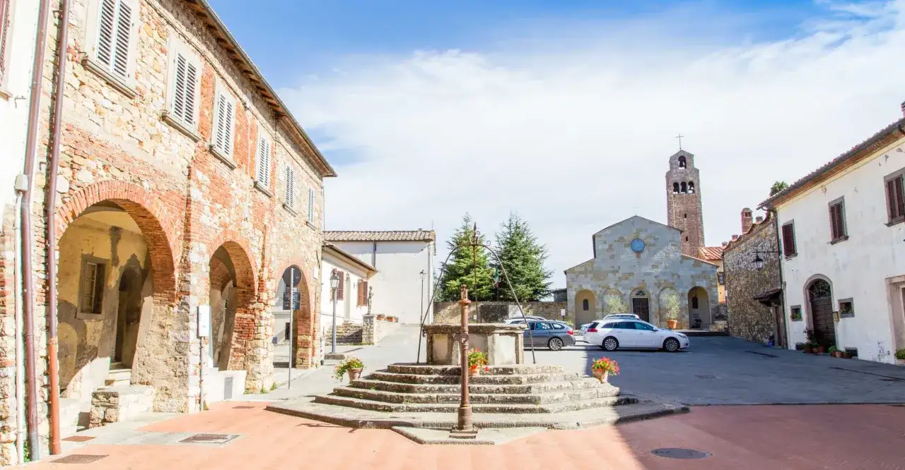 Piazza a Civitella Val di Chiana con pozzo antico, chiesa romanica e case in pietra.