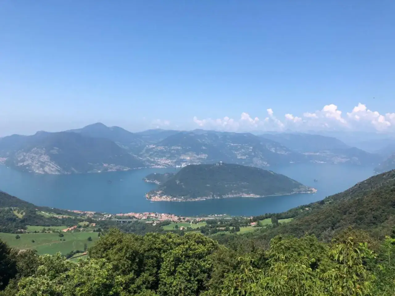 Vista panoramica dal passo del giogo su un lago alpino con un'isola e montagne sullo sfondo.