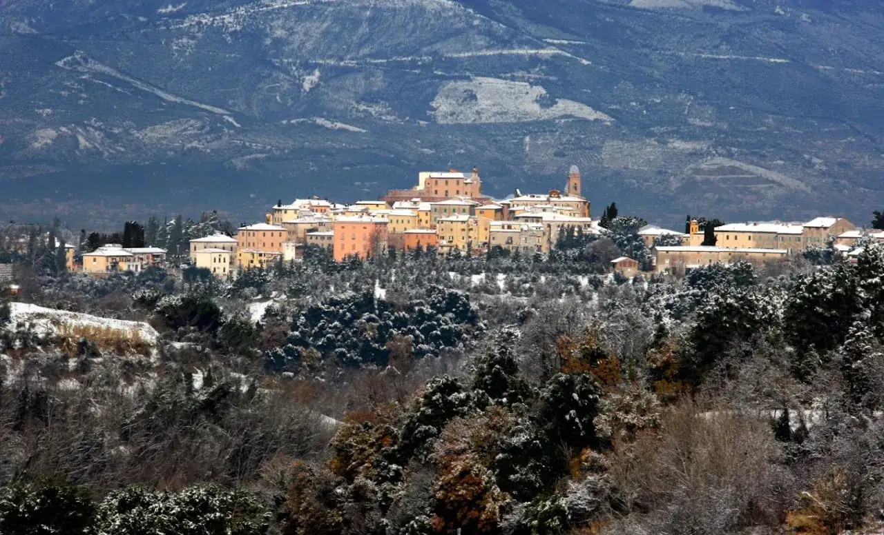 Borgo innevato con case colorate e montagne sullo sfondo. Scopri cosa vedere a Casciana Terme in questa suggestiva vista invernale.