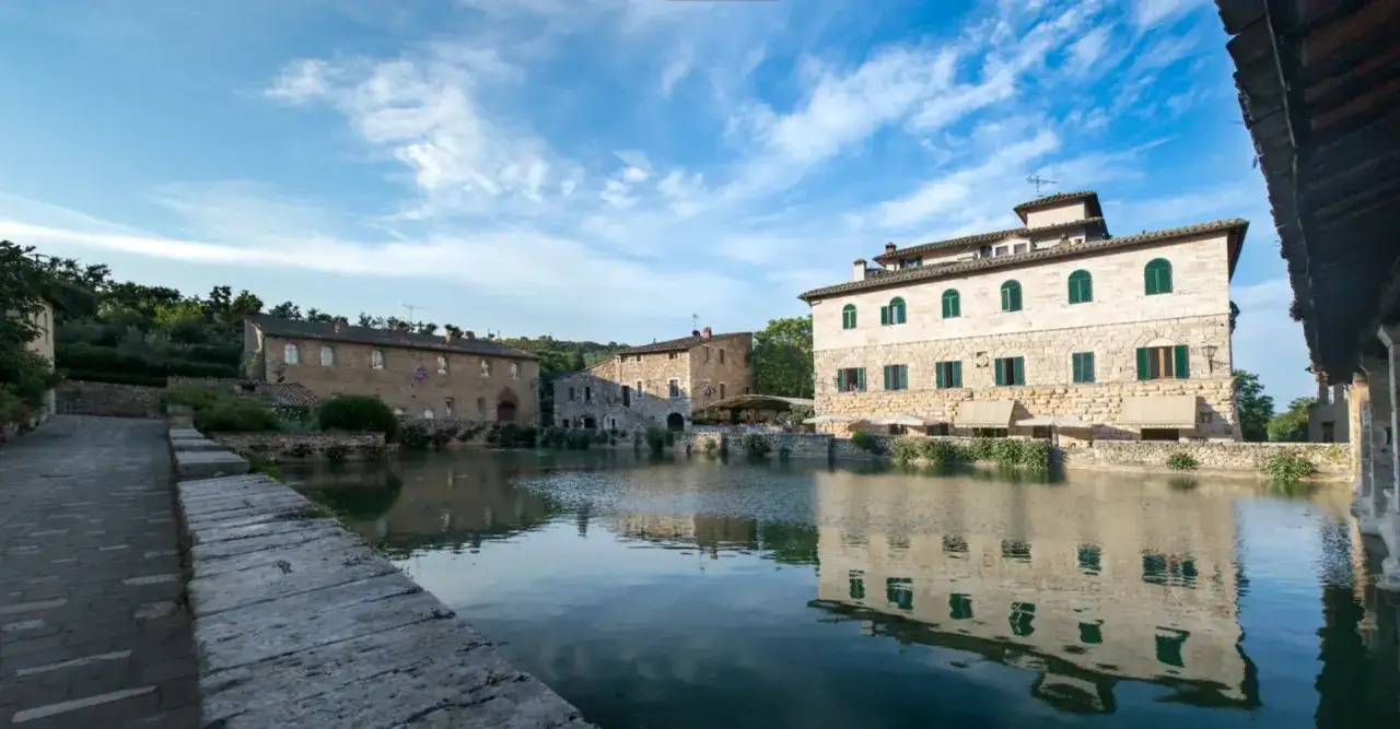 Bagno Vignoni, un luogo dove ci si può bagnare nelle acque termali, con edifici storici che si specchiano nel bacino.