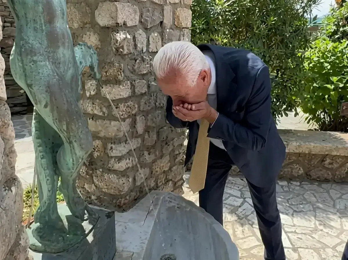 Uomo in abito scuro beve da una fontana artistica a San Carlo Terme.