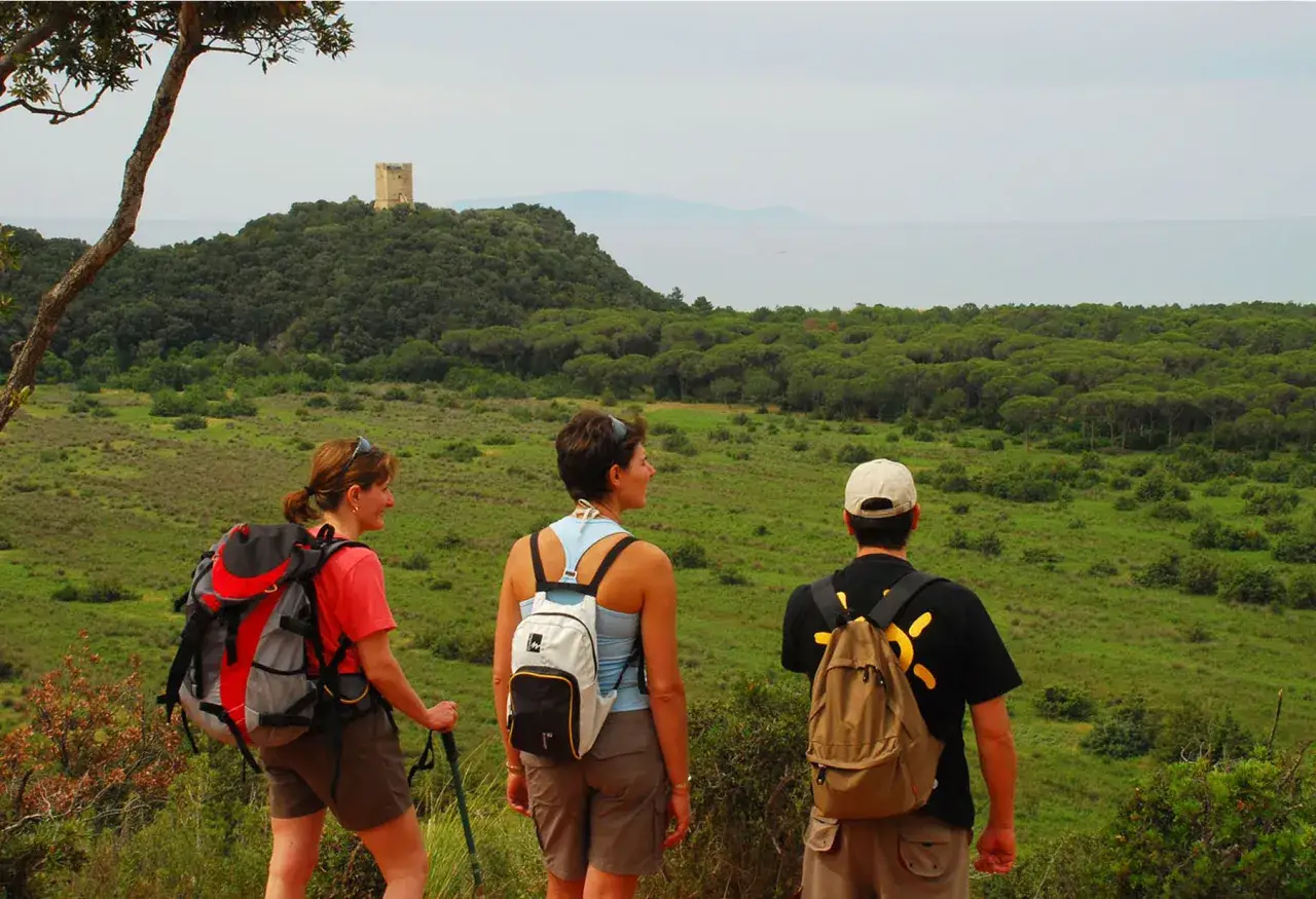 Tre escursionisti ammirano il panorama del Parco dell'Uccellina, con una torre in lontananza.