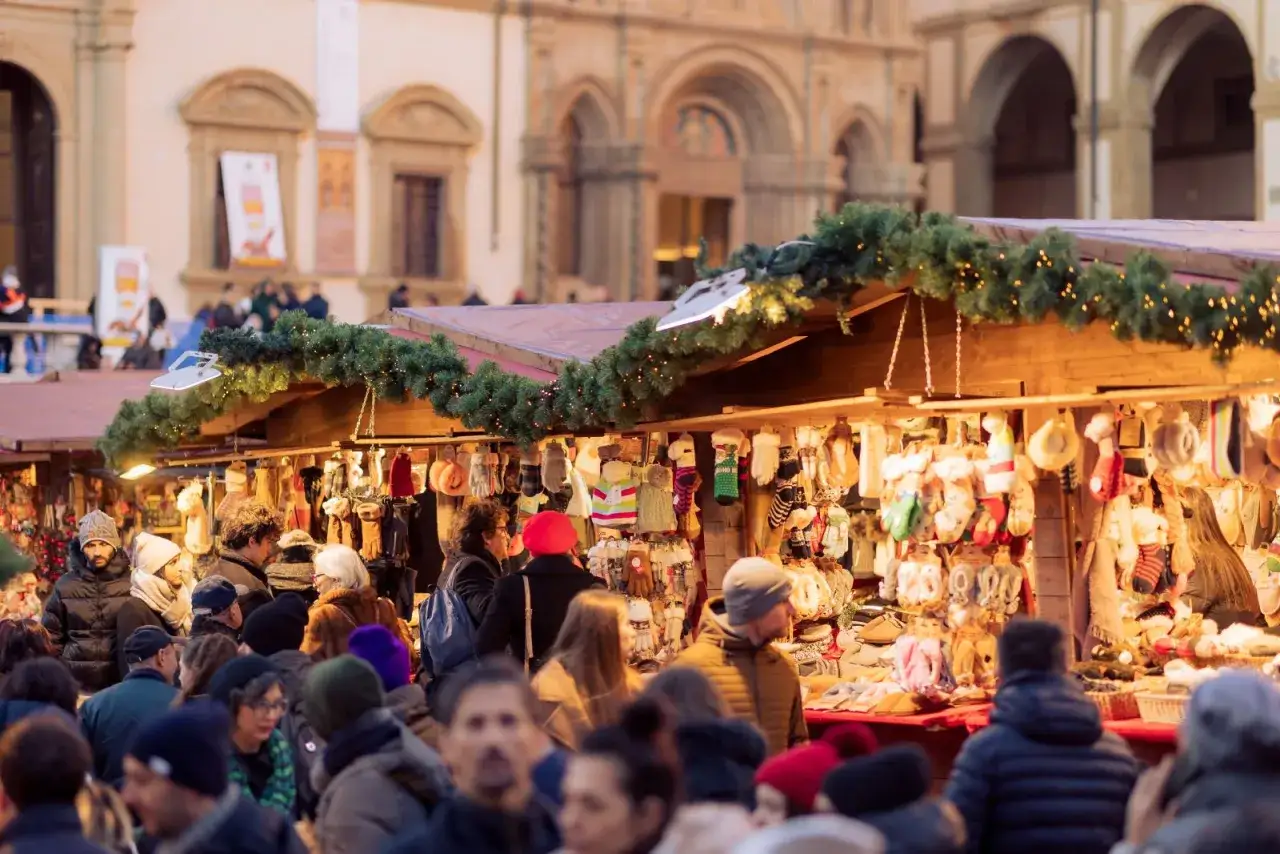 Mercatino natalizio in Toscana, con bancarelle addobbate di luci e ghirlande, piene di guanti e cappelli colorati.