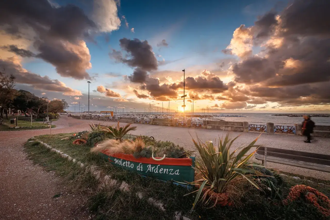 Tramonto sul lungomare di Livorno, con un'antica barca trasformata in fioriera e il porto sullo sfondo.