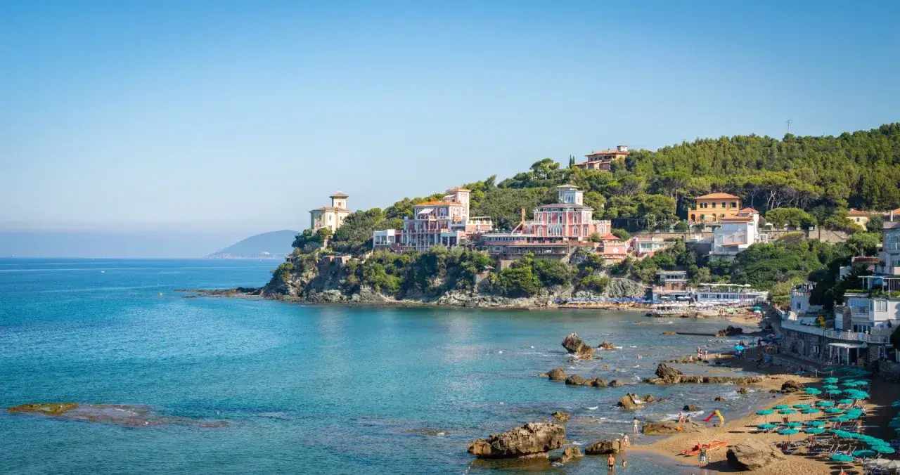 Splendida vista di Castiglioncello, Italia, con ville storiche sulla scogliera e una spiaggia affollata baciata dal sole.