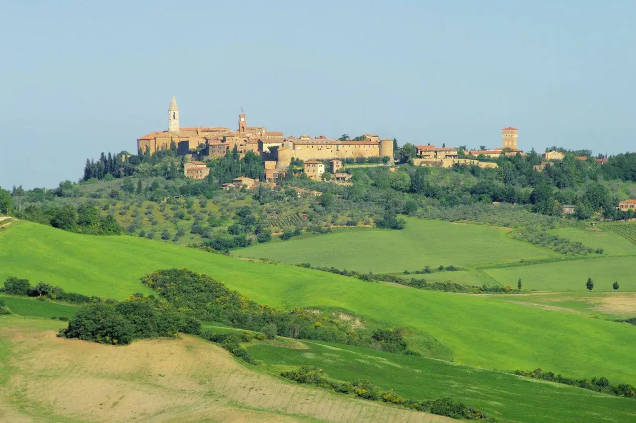 Borgo medievale in Valdichiana, con colline verdi e campi coltivati sotto un cielo azzurro.