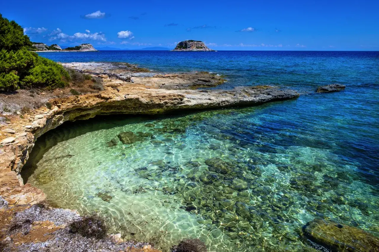 Acque cristalline e rocce dorate su un tratto di costa dell'isola di Pianosa, con un isolotto in lontananza.