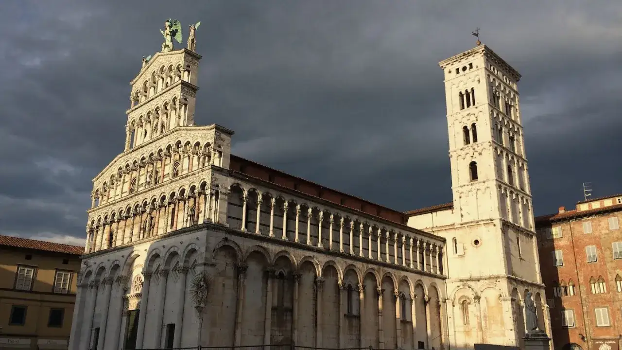 La chiesa di San Michele a Lucca, con la sua facciata riccamente decorata e il campanile imponente, si staglia contro un cielo drammatico.