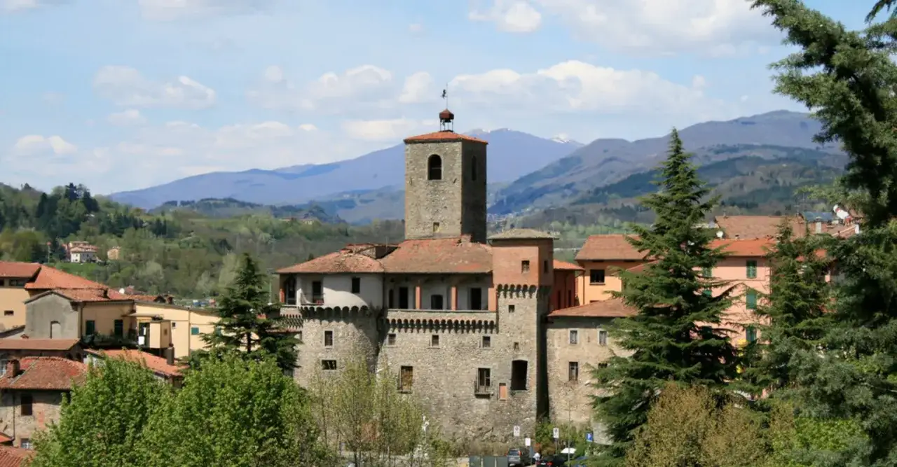La rocca ariostesca domina il borgo tra colline verdi e montagne azzurre, un antico baluardo che racconta storie.