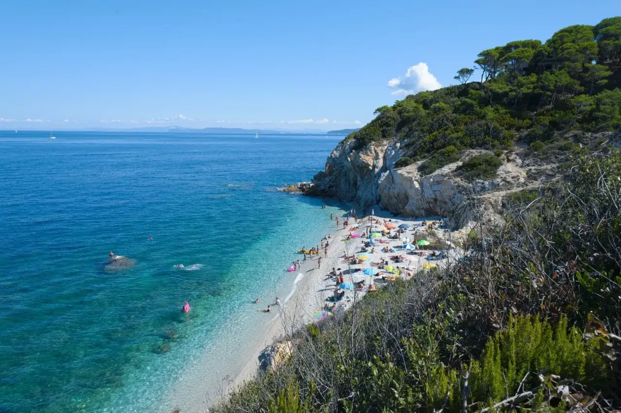 Spiaggia affollata a Marina di Campiglia, con bagnanti sotto ombrelloni colorati e gente che nuota nelle acque cristalline.