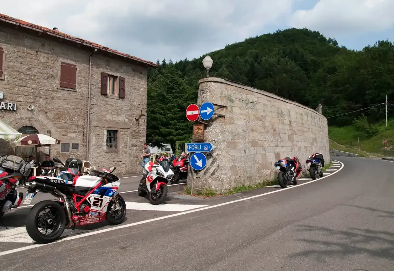 Motociclette sportive parcheggiate al Passo del Muraglione, con un edificio in pietra e una strada tortuosa sullo sfondo.