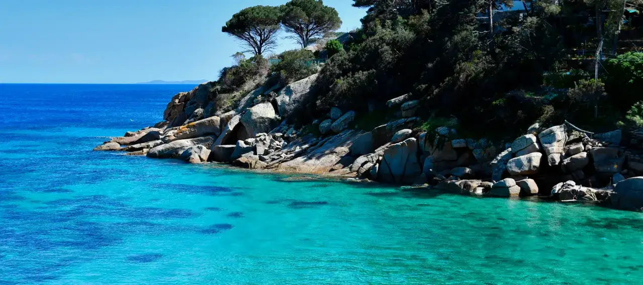 Acque cristalline e scogliere rocciose a Porto Santo Stefano, mare azzurro intenso sotto un cielo limpido.