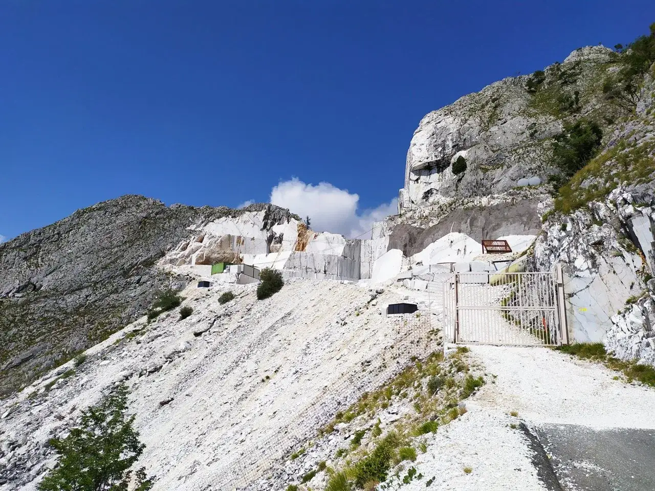 Cava di marmo con un cancello bianco. Il paesaggio montuoso ricorda un passo del vestito, con rocce bianche e verdi.