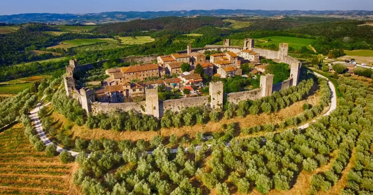 Un incantevole borgo toscano fortificato, circondato da uliveti e colline verdi, appare maestoso sotto il sole.