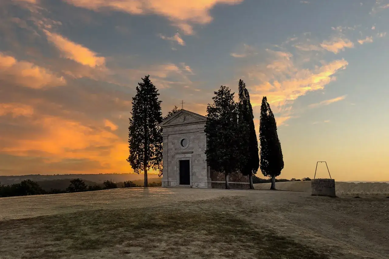 Iconica chiesetta Val d'Orcia al tramonto, con cipressi e cielo infuocato.