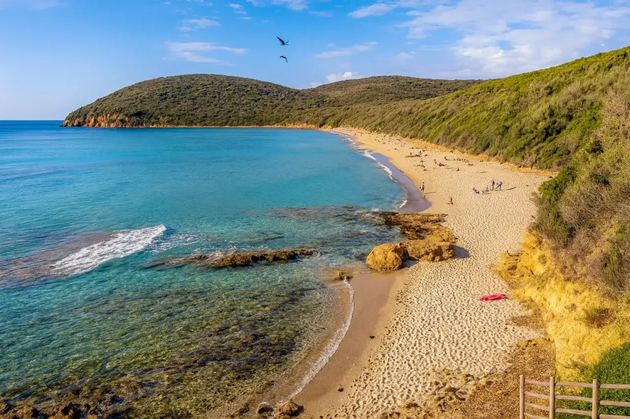 Spiaggia di Cala Martina con acque cristalline, sabbia dorata e colline verdi che la abbracciano. Un paradiso naturale.