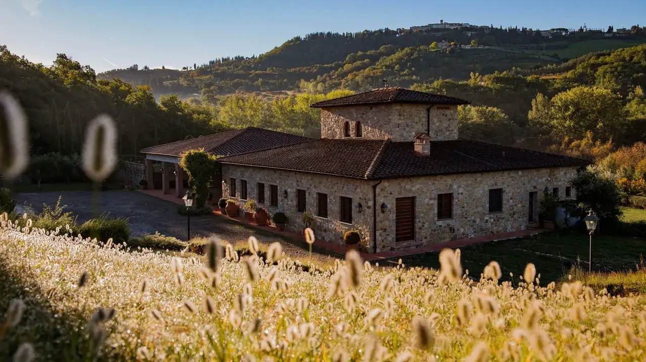 Un casale in pietra sulla strada dei castelli del Chianti, immerso nel verde delle colline toscane al tramonto.
