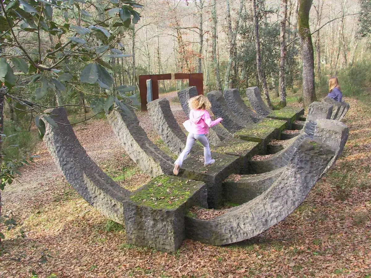 Bambina corre su una scultura in pietra nel Chianti Sculpture Park. Altre opere d'arte e alberi sullo sfondo.