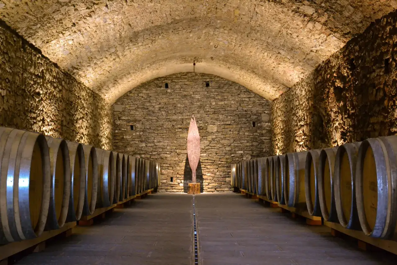 Cantine in pietra con botti di legno, un'installazione artistica al centro. Perfetto per una visita cantine Chianti.