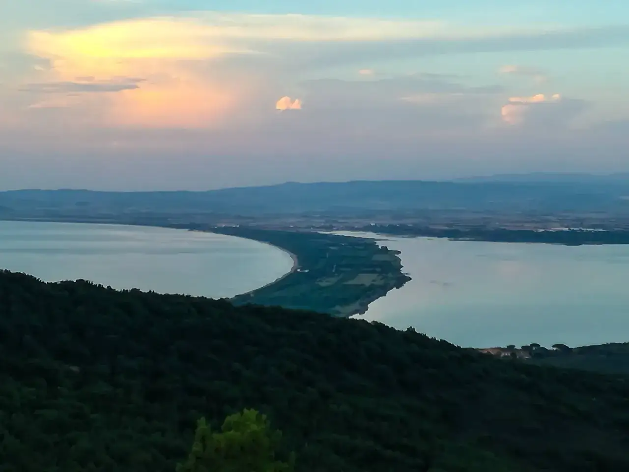 Tramonto sulle acque calme, con una lingua di terra verde che divide il lago. Un paesaggio che ispira i passionisti argentario.